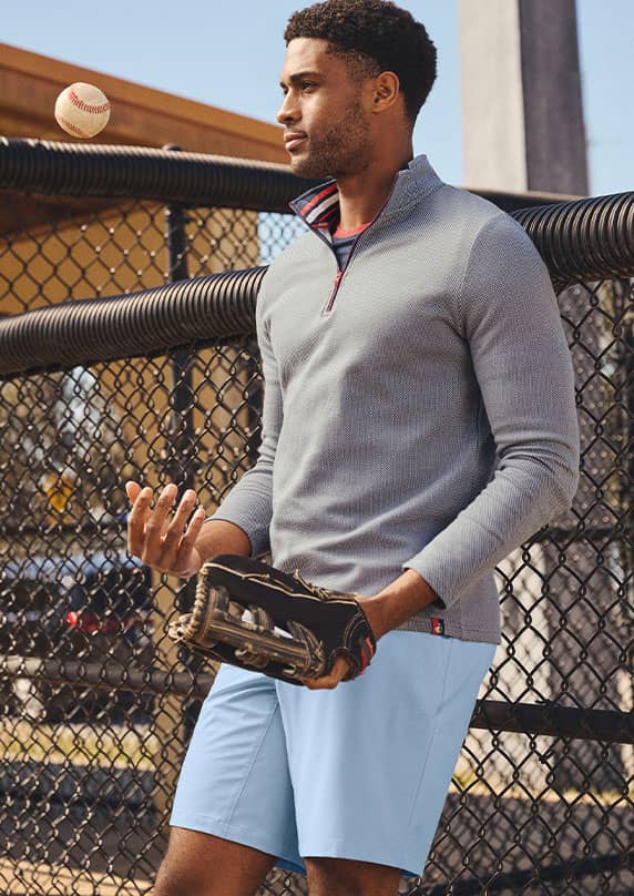 Man outside wearing a grey pullover playing baseball